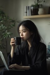 Fototapeta premium Contemplative young woman enjoying a warm drink while working on a laptop in a cozy, plant-filled room, embodying a tranquil and focused atmosphere.