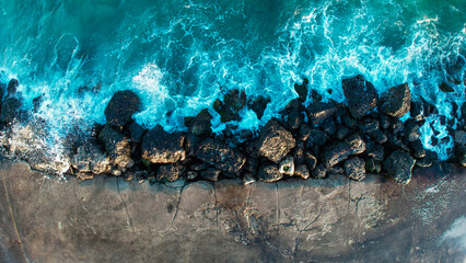 Aerial view of powerful turquoise ocean waves crashing against dark rocks on a rugged coastline, creating striking contrasts between vibrant blue water and the textured, rocky shore. © Grant