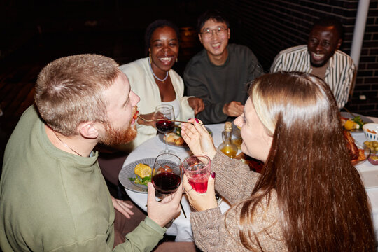 Multiethnic group of adults enjoying dinner party outdoors and couple clinking glasses, shot with flash - Powered by Adobe