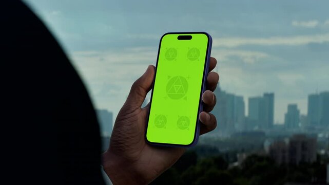 GREEN SCREEN CHROMA KEY Hand holding a phone with a city skyline in the background. Ideal for mockups of taxi, betting, or travel apps set in an urban environment