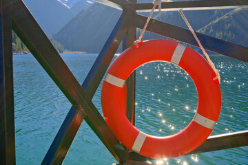 Orange life preserver ring against sparkling turquoise mountain lake water, safety equipment with scenic backdrop