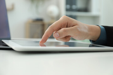 Businesswoman using tablet at white table indoors, closeup. Modern technology