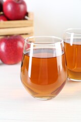 Fresh apple juice in glasses and fruits on white wooden table, closeup