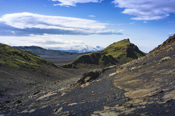 Hiking Laugavegur trail through black volcanic rocky desert with dramatic landscape, steep hills, valley and scenic look to the Eyjafjallajökull glacier on distant during beautiful summer day, Iceland