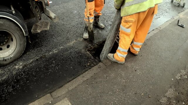 Roadwork team cleaning a road gully on a busy street during the early morning hours in the city