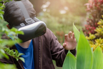 Fototapeta premium Asian highschool boy explores nature outside the classroom, observing trees and plants by using VR headsets with immersive technology to study details of leaves and bark up closely, soft focus.