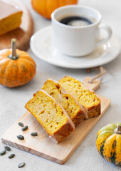 Pumpkin sweet bread or cake with icing on a wooden board on a light background with decorative pumpkins and a cup of coffee close up