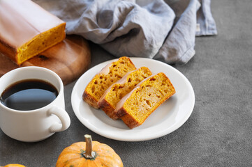 Pumpkin sweet bread or cake with icing on a plate on a dark background with decorative pumpkins and a cup of  coffee close up.