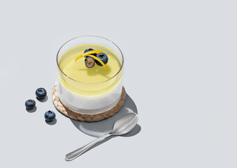 Lemon panna cotta with blueberries in a glass on a blue background with fresh berries, spoons and shadow.
