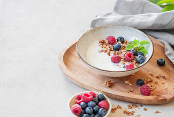 Granola with greek yogurt, raspberries and blueberries in a bowl on a wooden board on a white background with fresh berries.