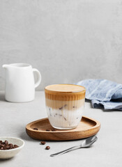 Dalgona coffee. Whipped instant coffee in a glass with ice on a wooden board on a gray background