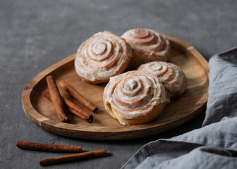 Fototapeta premium Sweet rolls with cinnamon and icing on a wooden board on a dark background with napkin.