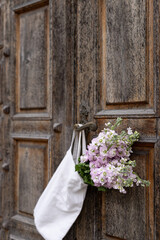 A rustic wooden door adorned with a bouquet of delicate flowers and a simple tote bag in a charming village setting