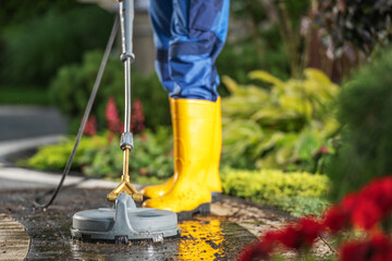 Person Using a High-Pressure Washer on a Garden Path Surrounded by Vibrant Plants in Sunny Weather