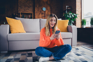Obraz premium Full length photo of lovely young girl sit floor hold gadget amazed dressed orange garment spacious house indoors room