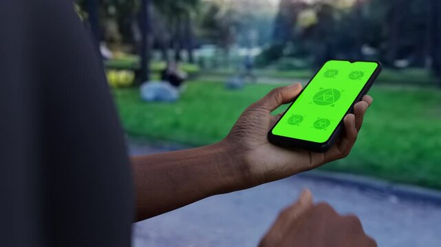 Black African-American young male using smartphone with a blank green screen. Maps, navigation, walking apps mockup. Vertical phone orientation