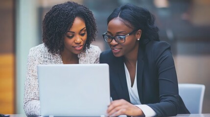 Two businesswomen working together on a laptop, training a new employee