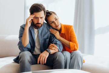 Obraz premium Couple portrait, beautiful young woman comforting bearded man, sitting on sofa at home, hugging