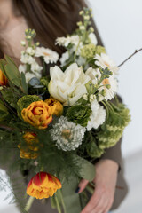 A beautiful spring bouquet adorned with bright flowers and lush greenery held delicately in the hands of a woman in a cozy setting