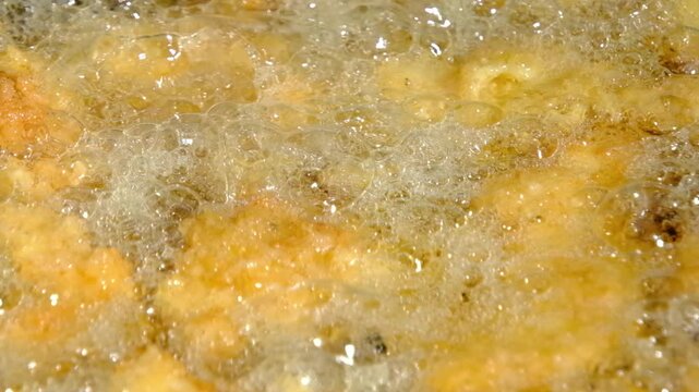 Extreme close up and slow motion while deep frying catfish nuggets or fish in batter and breadcrumbs in cast iron skillet or pan over firepit while camping outdoors