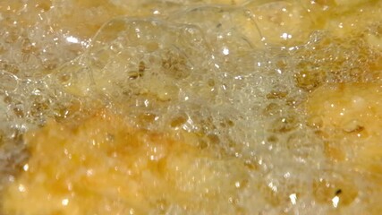Extreme close up and slow motion of oil boiling in cast iron pan while deep frying fish nuggets while camping outdoors - Powered by Adobe