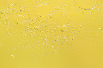 Essential oil bubbles on yellow background, macro view. Cosmetic product