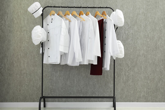 Chefs' uniforms on clothing rack near grey wall indoors