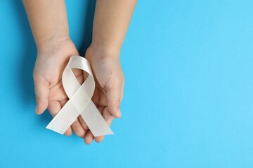 Child with white ribbon on light blue background, top view and space for text. Bone cancer and lung disease awareness