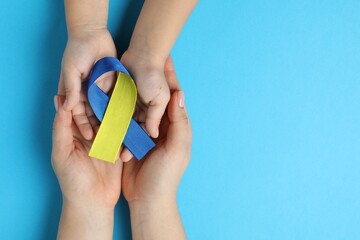 Woman with child holding yellow and blue ribbons on color background, top view. Down syndrome awareness