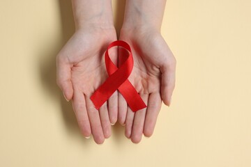 Woman with red ribbon on beige background, top view. HIV (AIDS) disease awareness