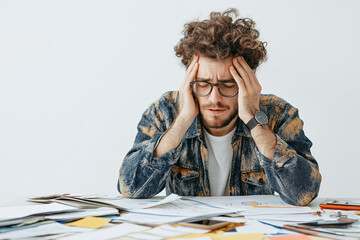 Frustrated man holding his head while looking at paperwork on a desk
