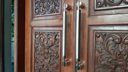 A Pair of Modern Stainless Steel Door Handles Combined With Unique and Antique Traditional Jepara Door Furniture, Central Java. 3D Flower Batik Carving Main Gate Living Room. Motif From Real Teak Wood