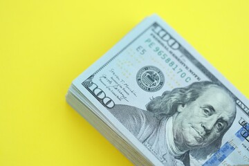 Big amount of hundred dollar bills in thick stack lies on bright yellow color paper background
