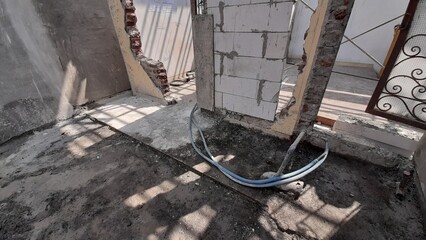 Damaged Wall Condition at Construction Site Renovation of Empty House in Shades During the Day. With a Practical Column Concrete Frame Structure and Unfinished Light Bricks. Abandoned Pipes and Hoses