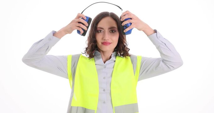 Woman construction worker puts on ear protection means on white background. Female in uniform prepares for work shift using specialized gear