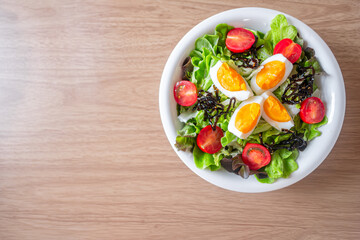 Green vegetable salad with leave,tomatoes,boiled eggs and microgreen on white plate on wooden table background