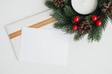 Elegant holiday wreath with blank card and envelope on white table