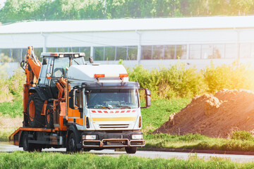 Tow truck transporting mini excavator on a sunny summer day on a countryside highway