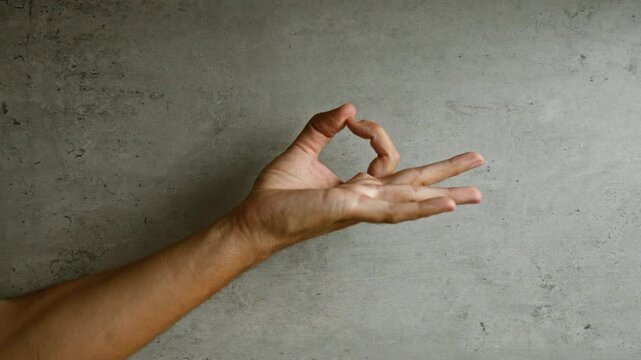 Hand making an ok gesture with fingers on a concrete background, highlighting gesture and simplicity.