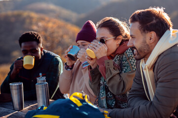 Group of friends sitting on the top of the hill at bench resting after hiking and drinking tea.