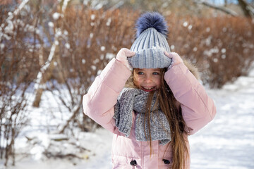 Happy laughing little girl in warm pink coat and grey knitted hat has fun and walking in snowy winter park. Children outdoor activities concept. Happy family holidays time. High quality photo