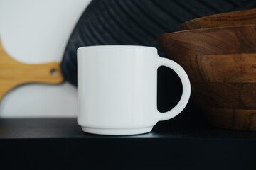 Simple white mug placed on a dark shelf beside wooden bowls in a cozy kitchen