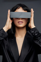 Naklejka premium Woman, black suit, black box a woman in a black suit holds a black box over her eyes, positioning her hands on the sides of her head, creating a mysterious and intriguing visual effect