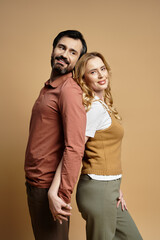 A middle aged couple stands back to back, smiling warmly in a cozy studio with soft lighting.