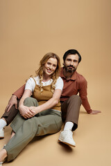 A joyful middle aged couple relaxes in stylish outfits against a soft backdrop.