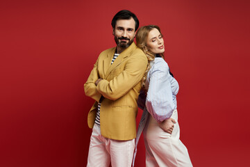 A middle aged couple stands back to back, blending styles and confidence in a vibrant setting.