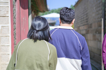 A Korean couple, a man in his 30s and a woman in her 20s, walks harmoniously through a historical building in Seoul, South Korea, wearing Hanbok.