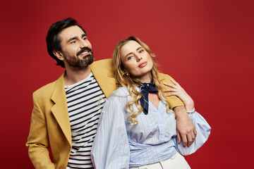 A stylish couple poses playfully in a vibrant red setting, exuding charm and confidence.