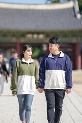 A Korean couple, a man in his 30s and a woman in her 20s, walks harmoniously through a historical building in Seoul, South Korea, wearing Hanbok.