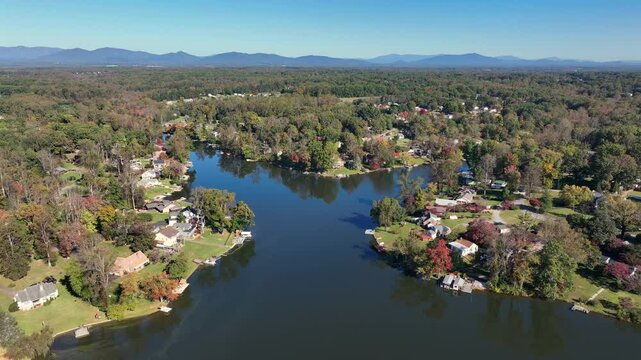 Aerial flyover Timber Lake in suburb neighborhood during sunny day. Autumn season with mountains in Background. Wide shot. Virginia, USA.